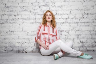 Young beautiful caucasian woman student is sitting on the floor near a white brick wall. Girl with