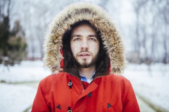 Portrait, close-up of a young stylish man with a beard dressed in a red winter jacket with a hood