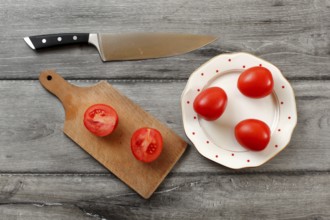 Table top view on three tomatoes on white porcelain plate with red dots, cutting board with tomato