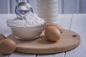 Very close up view eggs flour in bowl scoop bottle of milk on white painted old wooden board food