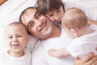 The father with three children in white laughing and playing on the bed