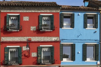 Close-up of red and blue houses with classic shutters and rustic façade, Burano, Venice, Veneto