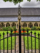 Iron gate in front of a garden in the monastery courtyard with well-tended flowerbeds and Gothic