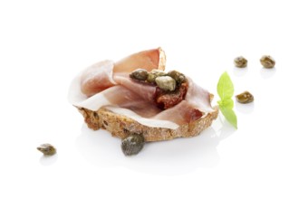 Luxurious canape background. Ciabatta slice with prosciutto, dry tomato and capers isolated on