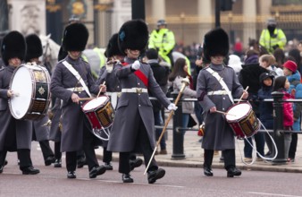 A parade of British guards in ceremonial uniform with black bearskin hats and flags marching in the