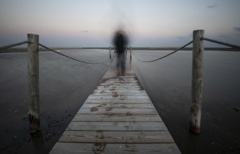 An unrecognised person walking like a ghost at a wooden pier