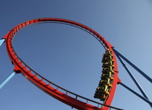 People on a dangerous Rollercoaster Ride in an amusement park against a blue sky