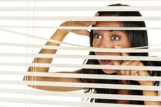 A young woman watches something through the blinds of her window Austria