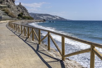 Promenade with wooden railings by the sea in front of the village with blue sky and sea, Castillo