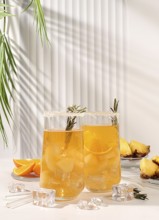 Cold homemade cocktail or lemonade with rosemary, orange, ice and pineapple on a sunny table, Detox