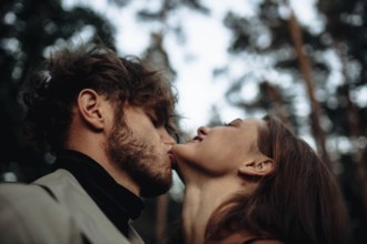 A couple sharing a romantic kiss in a forest setting