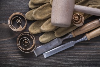 Pair of brown leather gloves firmer chisels wooden hammer and shavings on vintage wood board