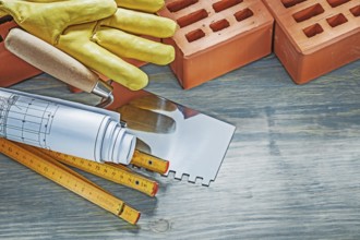 Red bricks working gloves blueprints wooden meter palette plastering trowel on wood board