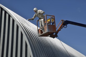 Tradesman spray painting the roof of an industrial building, Greymouth, South Island