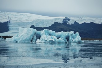 Icy blue icebergs mirrored in calm water amidst a vast glacier and mountainous backdrop, iceberg,