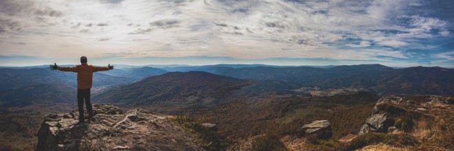 Panoramic view of mountain valley. Young man standing with hands widespread trying to embrace whole