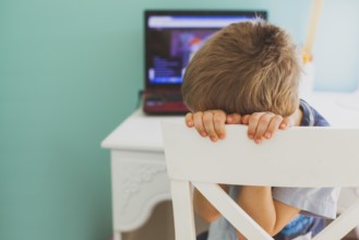 The sad little boy sits in front of laptop and doesn't want to look lesson. Concept of boring