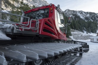 Tracked snow groomer with huge tracks in a winter scenery with the snowy austrian alps and forest