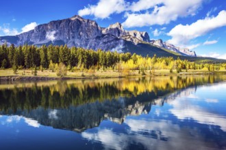 Concept hiking. Canmore, near Banff. Red-orange trees and jagged mountains are reflected in the