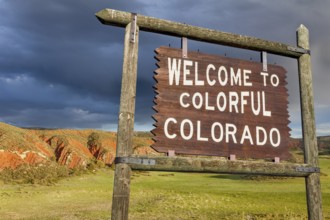 Welcome to colorful Colorado roadside wooden sign with red sandstone cliff in background