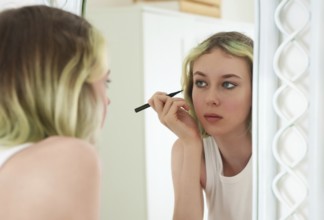 Teenage girl doing makeup with black eyeliner