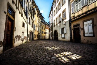 Narrow alley in the old town of Colmar with cobblestones and historic buildings under a blue sky in