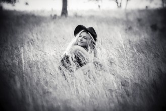 Young woman sitting in high grass in summertime in black and white