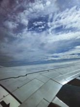 Aircraft wings under a wide sky with dramatic cloud formations, the return flight from holiday