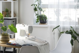 Sewing machine on a round table in the white interior of the house near the window with a