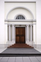The entrance of a newly built and modern church with an entrance door with a round arch and white
