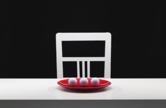 Three white golf balls on the red plate. White old chair and white table in the dark room