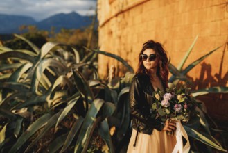 Bride in a beautiful pastel dress and sunglasses holds a bouquet of flowers in her hands against