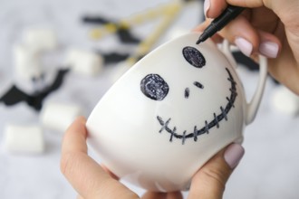 Female hands paint on white cup scary jacks face DIY for kids Halloween home activities Holiday art