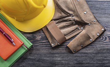 Leather tool belt notepads pen protective building helmet on wooden board construction concept