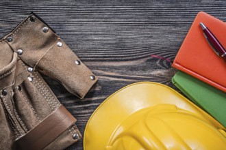Leather building belt note-books pen yellow hard hat on wooden board top view construction concept