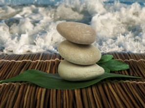 Stacked stones on wooden base for spa and green leafs. Waves on the background