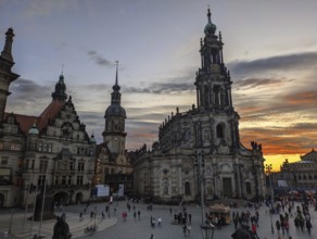 Crowded plaza with historic buildings at sunset, showcasing ornate architecture under a twilight