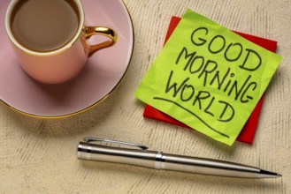 Good Morning world cheerful and positive memo - handwriting on a sticky note with cup of coffee