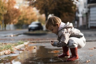 Little girl in red rainboots playing in puddle after rain. Happy fall childhood activity