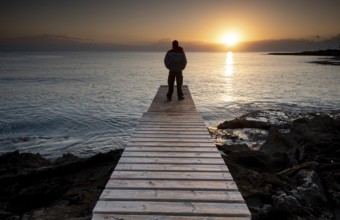 Person standing at the edge of a wooden pier in the sea at sunrise, People active outdoors enjoy