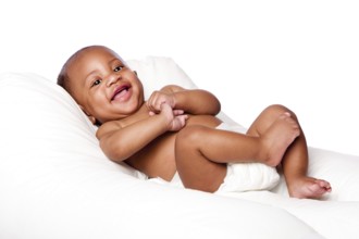 Happy cute smiling laughing African baby infant laying wearing diapers on soft bed, isolated,