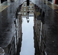 Street scene with puddle reflecting brick buildings and lanterns creates urban and wet ambience,