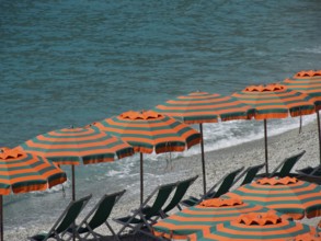 Row of striped parasols on a pebbly beach with a view of the sea and gentle waves, Monte rosso,