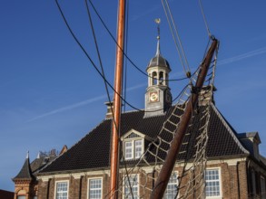 Building with clock tower and sailing mast in the foreground under a blue sky, empty, East Frisia,