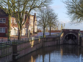 Urban scene with canal lined with trees and buildings. Bridge and reflection visible in the water,