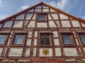 Historic half-timbered facade of a house with coat of arms under blue sky and clouds, waldeck,
