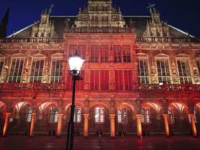 Impressive gothic building with red lighting and a lantern in the foreground at night, Bremen,