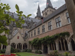 Historic monastery courtyard with Gothic architecture and surrounded by gardens under a cloudy sky,
