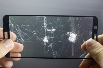 Broken protective glass of smartphone with cracks in hands on black background. Damaged protective
