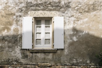Old window with wooden white painted open shutters in weathered plaster wall